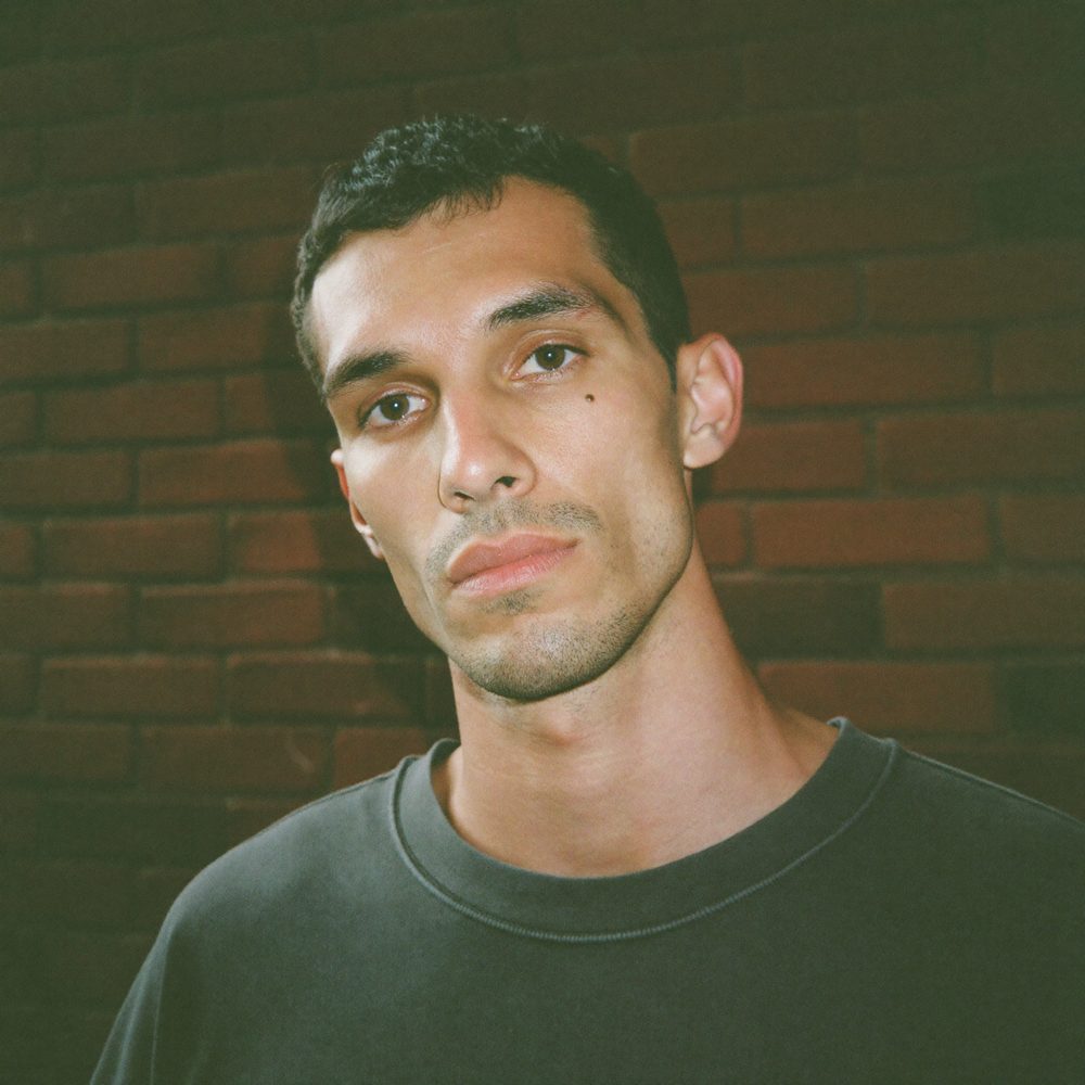 Retrato de un hombre con camiseta oscura delante de una pared de ladrillo